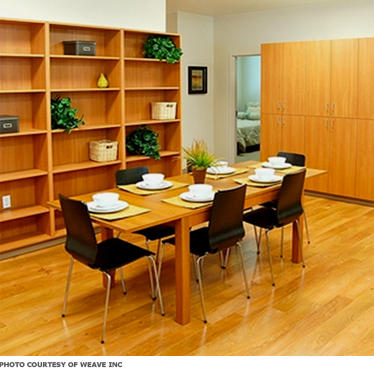 A dining room with wood floors and table, as well as simple hard chairs, all easy to clean.
