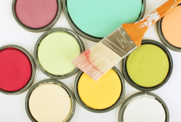 A paint brush sitting on several bright buckets of paint.